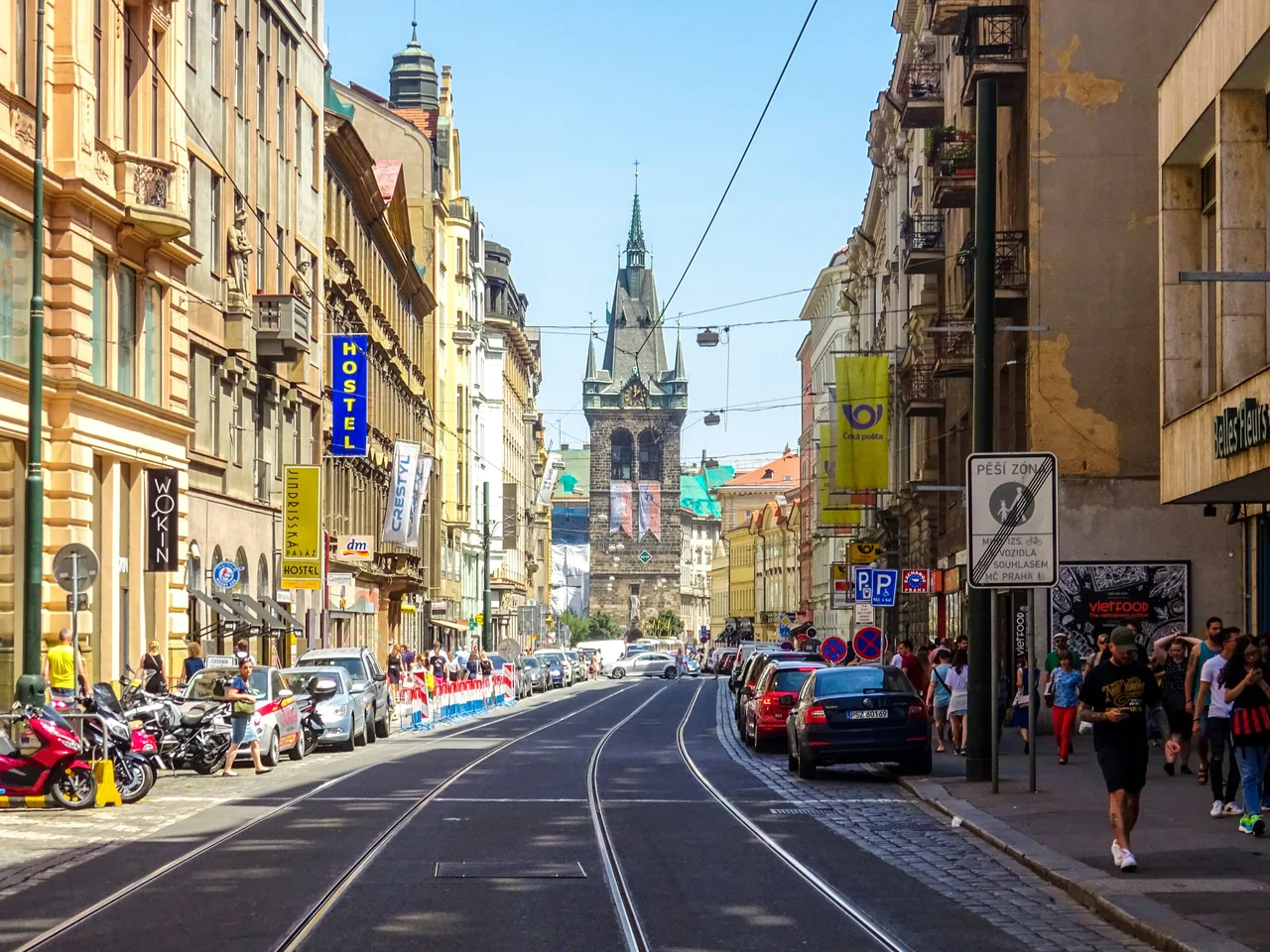 Tramvajové koleje mezi historickými pražskými domy směřují ke vzdálené věži.