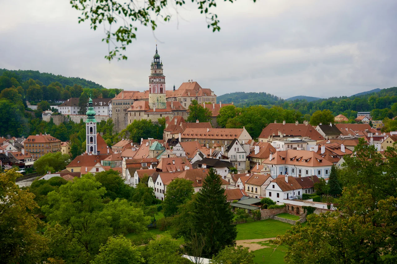 Panorama Českého Krumlova s červenými střechami, zelení a zámeckou věží.