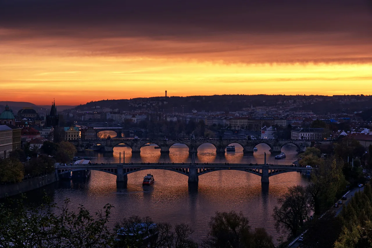 Pražské mosty přes Vltavu pod oranžovou oblohou při západu slunce.